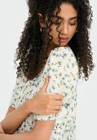 Haut à imprimé floral avec des manches courtes, présentant un fond crème et des fleurs bleues. Tissu doux avec une coupe décontractée et une légère texture.