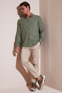 Camisa verde de botones, pantalones beige de corte ajustado y zapatillas multicolores. Texturas suaves, ajuste relajado y diseño de cuello clásico.