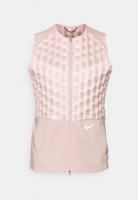 Jasnoróżowa bezrękawnik z zamkiem błyskawicznym, z pikowaną górną częścią i białym logo Nike po prawej stronie na dole.