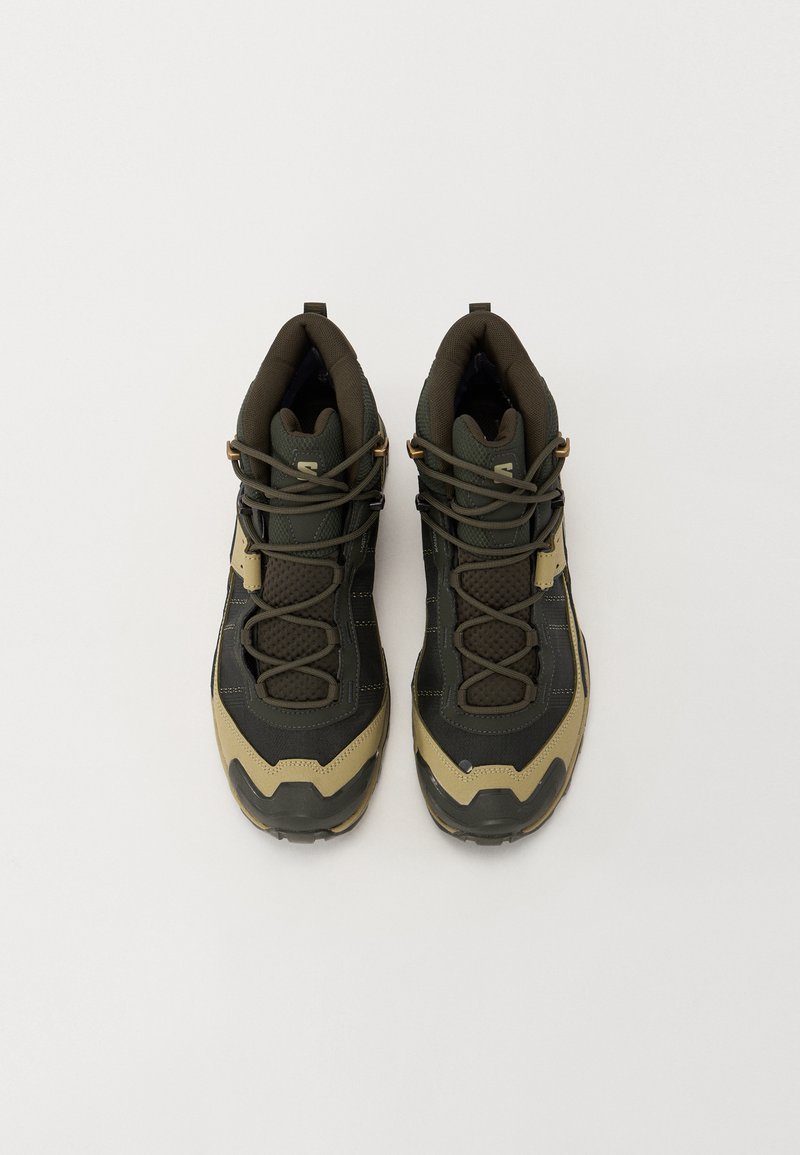 Dark green and tan hiking shoes with textured fabric, padded collars, and lacing system. Features rubber soles and contrasting design elements.
