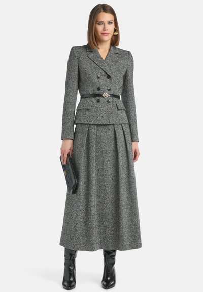 Siva tweed sakoo z dvojnim gumbnim zapenjanjem z peplum pasom, v kombinaciji z ujemajočo dolgo krilo. Črn pas in torbica poudarita obleko.