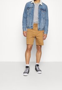 Veste en denim avec col en shearling, t-shirt gris, short cargo marron et baskets montantes noires avec lacets blancs.