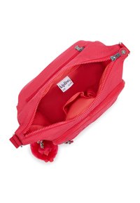 Röd tygpouch med dragkedjor, en pom-pom-accent och en slät textur. Inuti finns en monogrametikett och en ficka.