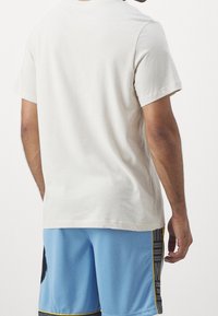 Camiseta de manga corta en color beige claro con un corte clásico, combinada con pantalones cortos deportivos azules que cuentan con un acento negro y un patrón de rayas.