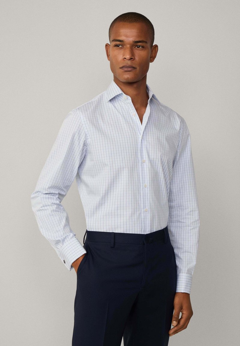 Camisa de button-up a rayas azul claro con cuello extendido y mangas largas, combinada con pantalones oscuros de color navy. Fabricada en una mezcla de algodón, con un ajuste casual.