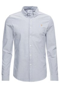 Ljusblå button-up skjorta med krage, långa ärmar och en liten gyllene logotyp på bröstet. Tillverkad av ett slätt, vävt tyg.