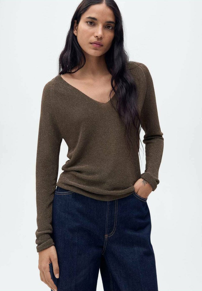 Maglione marrone a maniche lunghe con scollo a V, realizzato in un materiale testurizzato, abbinato a jeans di denim scuro.