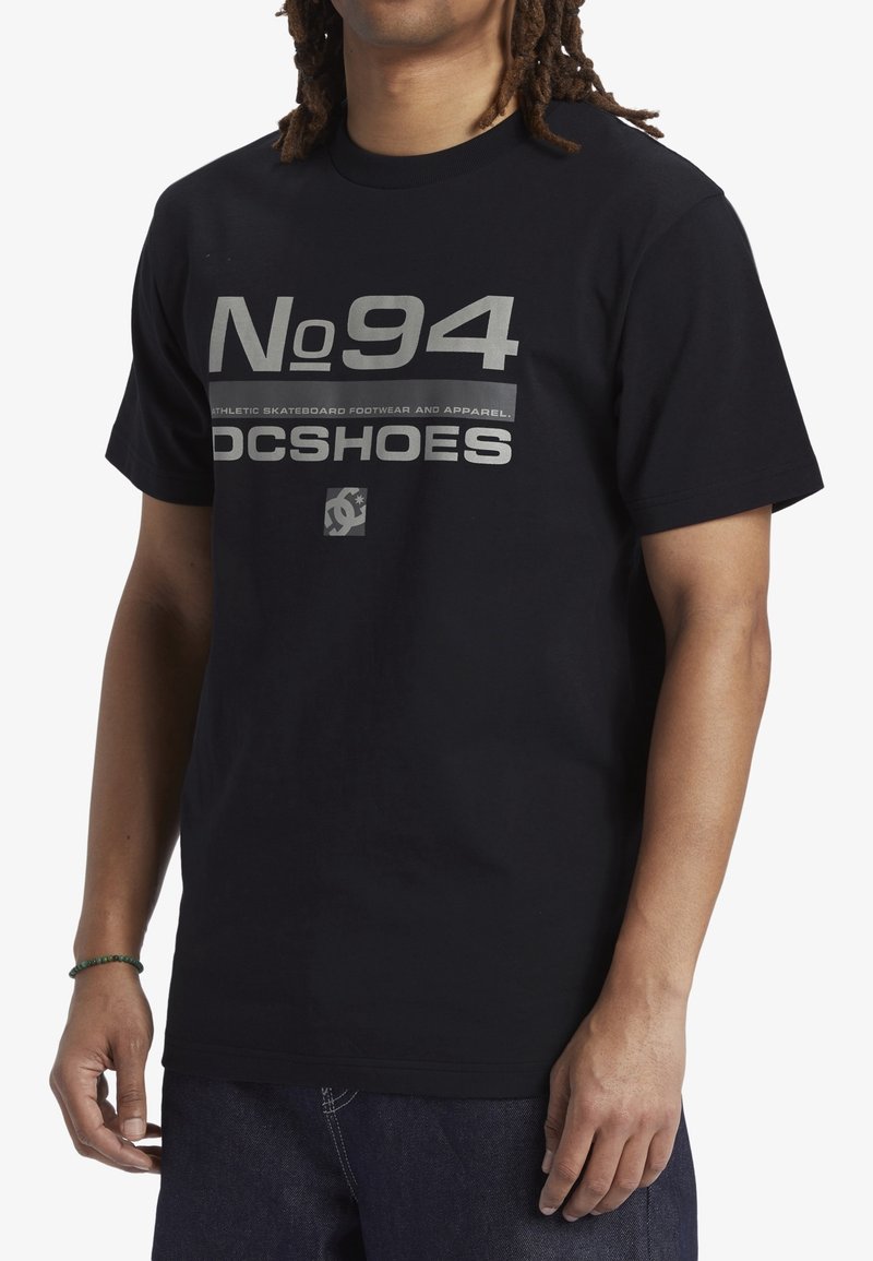 Svart bomullströja med fet vit grafisk text "No 94" och "DC SHOES", med korta ärmar och standard passform.