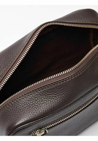 Brun läderväska med texturerad yta, dragkedjestopp och bronsdetaljer. Har ett rymligt inre med foder.