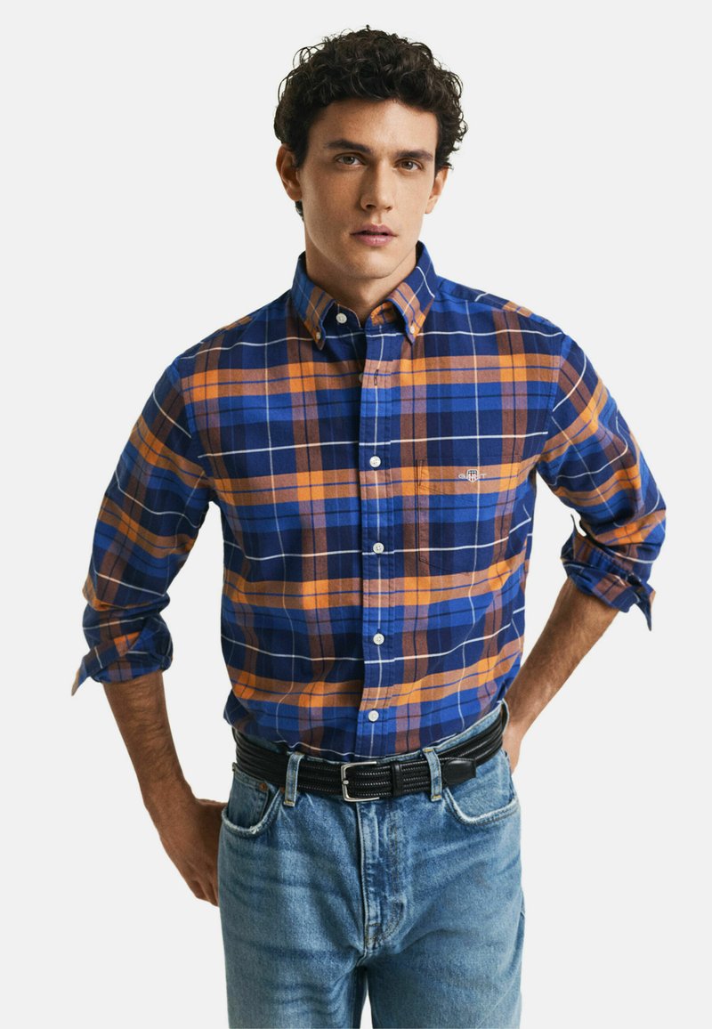Blauwe en oranje geruite shirt met een button-down kraag, voorzien van witte lijnen en een borstzak, gedragen met een zwarte riem en blauwe jeans.