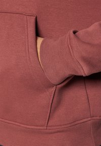 Felpa bordeaux con tasca laterale, caratterizzata da una texture morbida, polsini a costine e una vestibilità comoda. Enfasi sulle cuciture e sulle giunture.