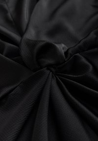 Black textured fabric gathered into a central knot, creating folds and shadows across the surface.