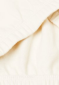 Tela de color crema con una textura suave y esponjosa. Presenta un borde ribeteado suave y una costura recogida, proporcionando una apariencia en capas.