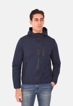 Giacca leggera blu navy con cappuccio, chiusura frontale con zip e due tasche laterali. Presenta una tasca sul petto con zip e dettagli neri. Texture liscia.