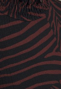 Svart tyg med en texturerad yta pryds av djärva, mörkröda zebraränder. Materialet är lätt och något skrynkligt, med en rynkad topp.