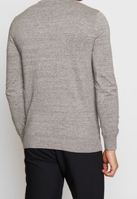 Grå sweater med strukturstickning, långa ärmar, ribbade muddar och fåll, med en rund halsringning. Bärs över svarta byxor.