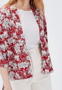Red floral kimono jacket with white outlines, short sleeves, and an open front. Worn over a white top and beige high-waisted pants.