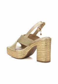 Sandalias de cuña doradas con una correa de tejido trenzado texturizado y un tacón grueso similar a una cuerda. Con tiras ajustables en la parte trasera y un acento metálico.