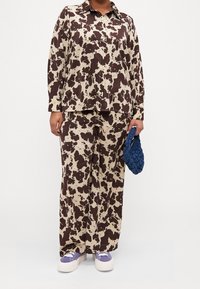 Set di blouse e pantaloni con stampa a macchie di mucca marroni e beige, abbinato a una borsa a tracolla blu in tessuto e sneakers viola. Tessuto morbido, stile button-up, vestibilità ampia.