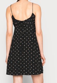 Vestido negro sin mangas con tirantes finos y estampado floral, presenta una parte posterior fruncida con un detalle de lazo. Tela suave y diseño hasta la rodilla.