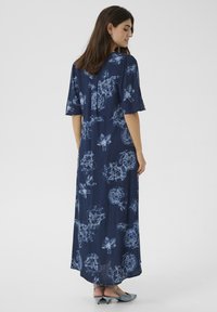 Tengerészkék virágmintás ruha rövid ujjakkal, texturált anyagból készült és hosszú sziluett jellemzi. Kiemelkedő részletei között van a világoskék virágminta.