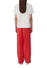 T-shirt en coton blanc associé à un pantalon rouge vif ample. La tenue est complétée par des chaussures blanches.