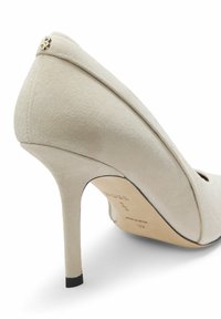 Scarpa con tacco alto in camoscio beige con punta appuntita, design scolpito, dettaglio nero sul tacco e logo dorato sul retro.