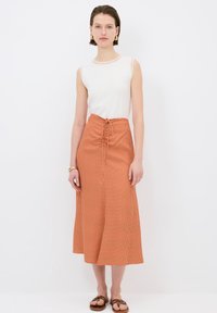 Top blanco sin mangas combinado con una falda midi a cuadros naranjas con cintura elástica. La falda tiene una textura suave y una silueta fluida.