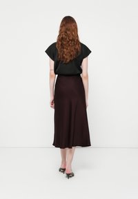 Top nero con maniche corte abbinato a una gonna midi bordeaux, texture liscia e sandali neri con tacco, visto da dietro.