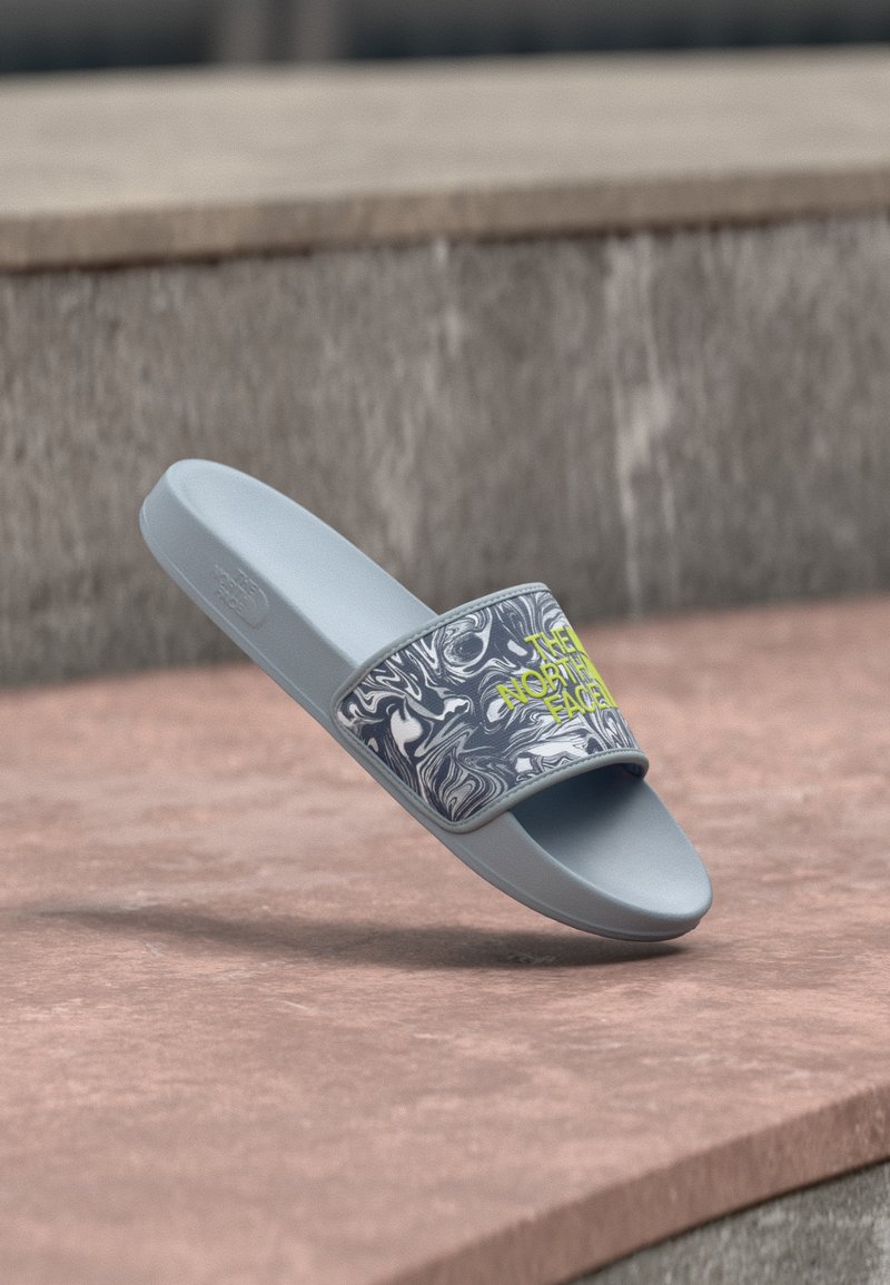 Γαλάζιο σανδάλι με λουρί σε σχέδιο μαρμάρου και κίτρινο λογότυπο «The North Face», ακουμπισμένο σε πέτρινη επιφάνεια.