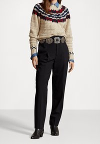 Suéter de punto beige con patrones en rojo y azul marino, combinado con pantalones negros de talle alto y un cinturón decorativo plateado. Botines negros de tacón.