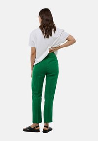 Un pantalon en lin vert à coupe décontractée, avec une taille élastique et des poches latérales, associé à un T-shirt blanc ample et des sandales noires.
