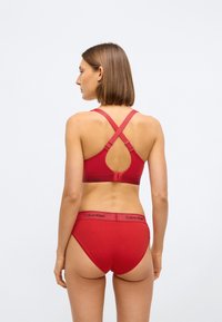 Rød Calvin Klein-bh med utskåret rygg og kryssede stropper, kombinert med matchende høyhælte truser som har logo-detaljer på midjebåndet.