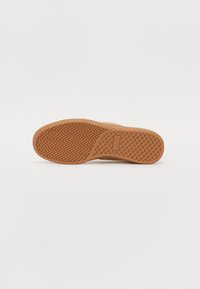 Brun gummi skosål med et zigzag-mønster og gittertekstur for greb, der har et centralt logo-detalje.