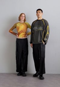 Spodnie: czarne, luźne z materiału z bocznymi akcentami. Bluzka: wzorzysta, z długim rękawem, łącząca odcienie żółtego i pomarańczowego, dopasowany krój.