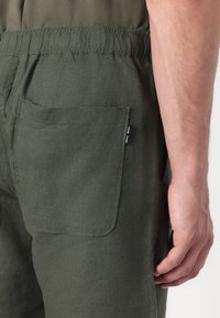 Pantalons en lin vert olive avec une taille élastique. Dotés d'une poche latérale et d'un tissu texturé. Design simpliste, adapté à un usage décontracté.