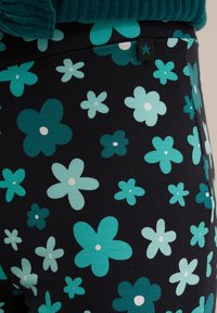 Crne tajice s cvjetnim uzorkom u različitim nijansama tirkizne i bijele boje. Sadrže male cvjetove s zaobljenim laticama i mekom teksturom.