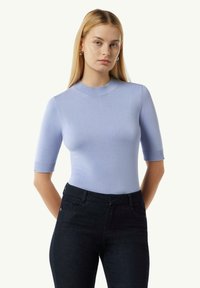 Jasnoniebieski sweter z krótkim rękawem, o wysokim dekolcie i prążkowanymi akcentami, w połączeniu z ciemnymi dżinsami; gładka faktura.