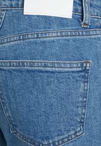 Vaqueros de denim en azul claro con detalle en el bolsillo trasero. Presenta una etiqueta de logo blanca con "CLOSED" en relieve. Incluye acentos de costura en contraste.