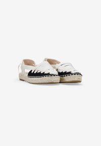 Zapatos espadrilles en blanco y negro con suela de yute trenzado, diseño plano y correas de tela entrelazadas. Textura suave y forma de punta redonda.