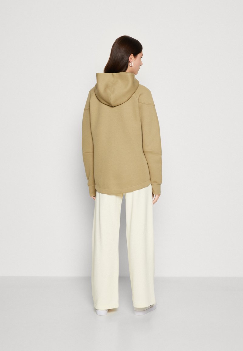 Khaki Kapuzenpullover mit Kapuze, mit lockerer Passform und abgeschrägten Schultern. Kombiniert mit lockeren weißen Hosen für einen schichten Look.