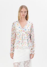 Blusa avvolgente floreale in tessuto leggero e trasparente, con scollatura a V, maniche lunghe e dettagli smerlati. Presenta motivi floreali multicolori.