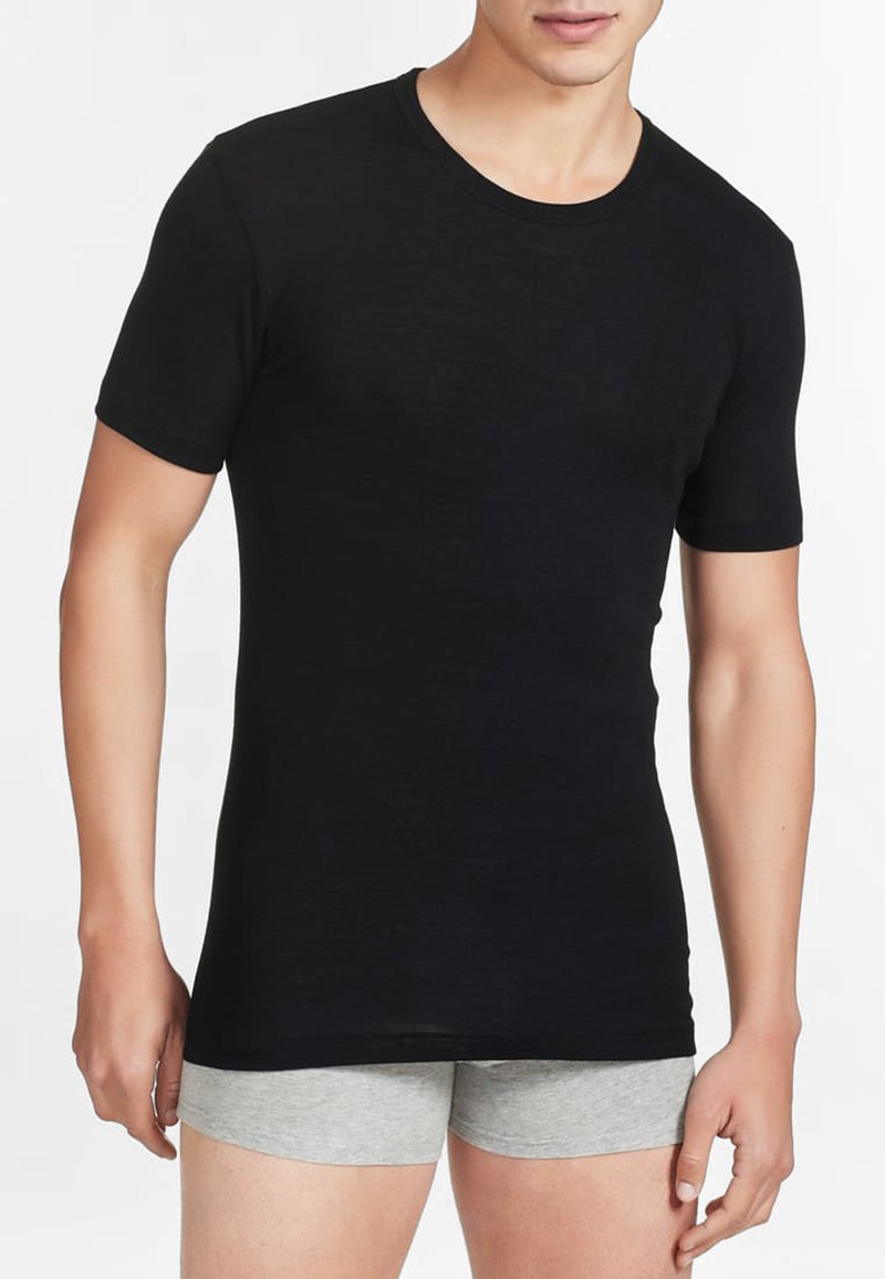 T-shirt nera a maniche corte realizzata in tessuto morbido, con scollo rotondo e design aderente. Indossata con pantaloni corti grigi.