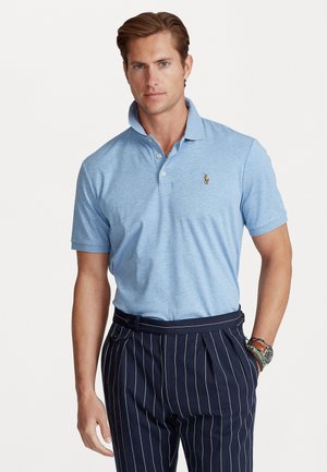 Svetlomodrá polo košela s klasickým golierom a vyšitým logom. V kombinácii s tmavomodrými nohavicami s prúžkom, ktoré ukazujú prispôsobený strih.