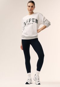 Helehall hall pusakaas "ASPEN COLORADO" musta trükitud, kombineeritud tumesiniste retuuside ja valgete keskmise pikkusega sokkidega, aksessuaarina hõbedased rõngas-kõrvarõngad.