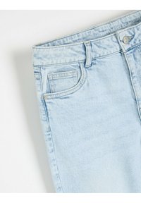 Jasnoniebieskie dżinsy z wysokim stanem, z zapięciem na guziki i przednimi kieszeniami. Materiał ma miękką, nieco wyblakłą strukturę.