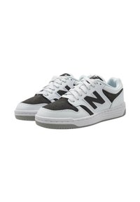 Sneaker bianca e nera con una tomaia in pelle liscia e suede. Presenta perforazioni, lacci piatti e una suola in gomma grigia. Dettaglio del logo in nero.