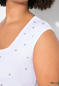 Top senza maniche bianco a coste con dettagli in strass argentati lungo le spalle e la parte superiore del torace, con scollatura a u e design aderente.