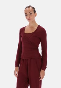 Bordeauxrode wikkeltrui met lange mouwen, een vierkante halslijn, gelaagde stijl en zachte textuur, gecombineerd met bijpassende bordeauxrode broek.