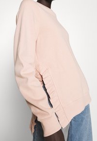 Lichtroze sweatshirt met geribde manchetten en boord, voorzien van gerimpelde zijaccenten. Zachte stof met een relaxte pasvorm en ronde halslijn.